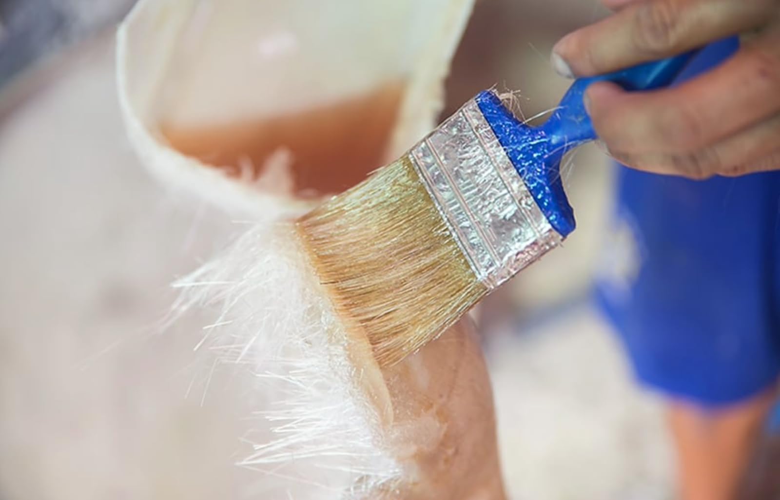 Person painting a surface of fiberglass with a brush.